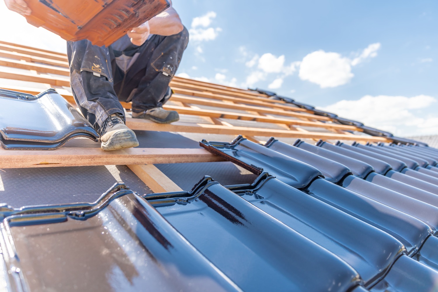 Dakdekker plaatst glanzende dakpannen op een nieuw dak tijdens woningrenovatie onder een blauwe hemel