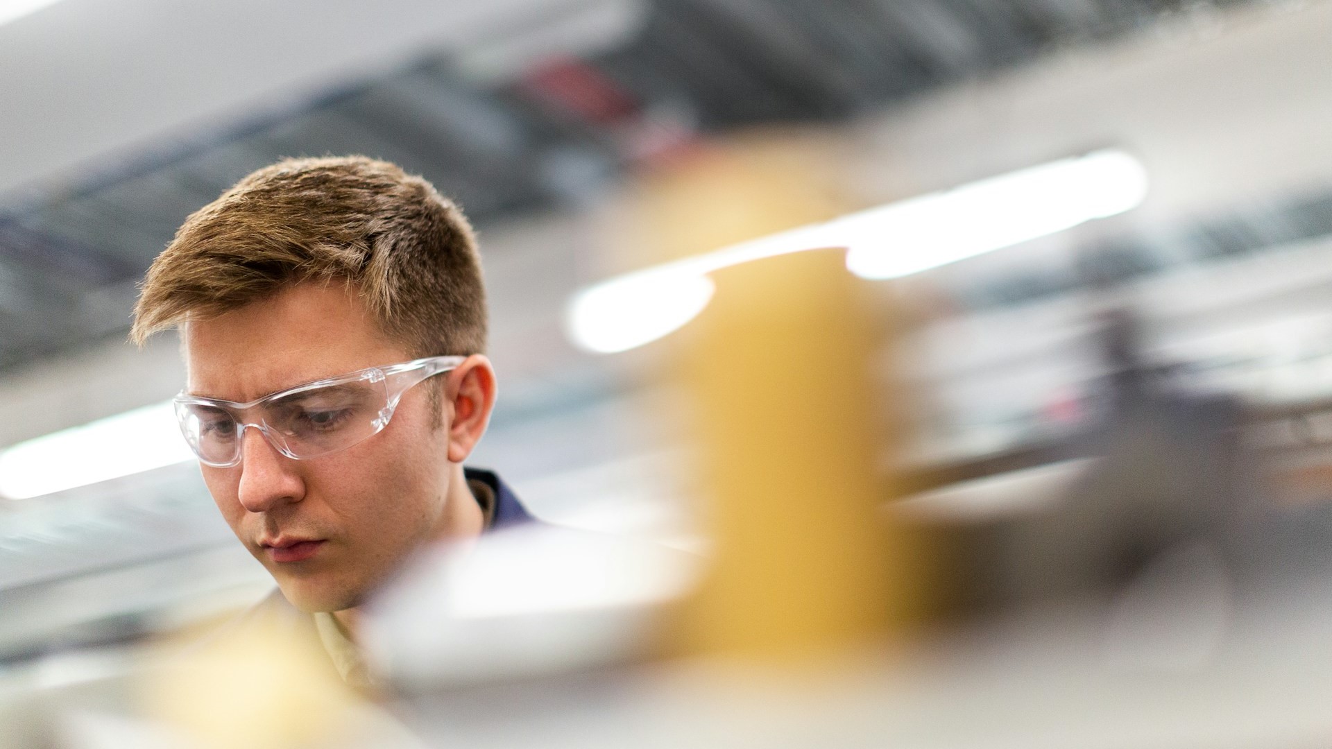 Jonge monteur met veiligheidsbril werkt geconcentreerd aan technisch apparaat in productieomgeving